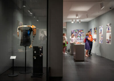 Steampunk Style Arm on display with four attachments and exhibition attendees viewing panels in the background