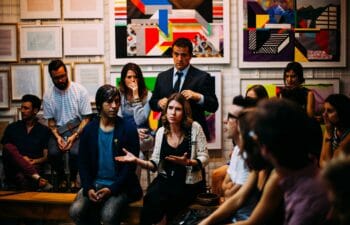 a woman talking in a group of people with a wall of artwork in the background