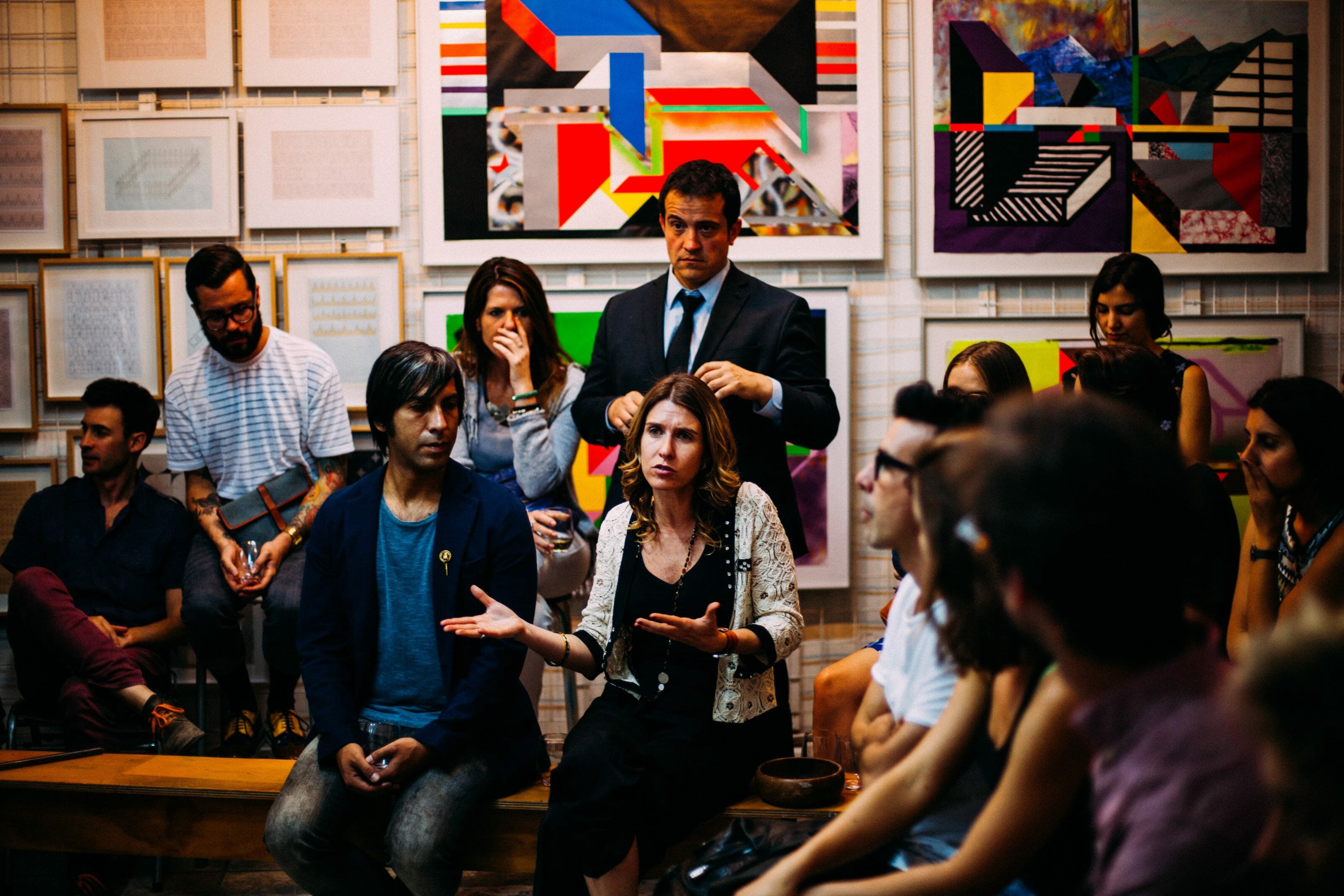 a woman talking in a group of people with a wall of artwork in the background