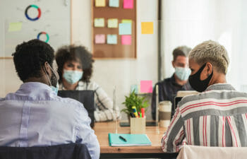 Four office workers around a table wearing masks