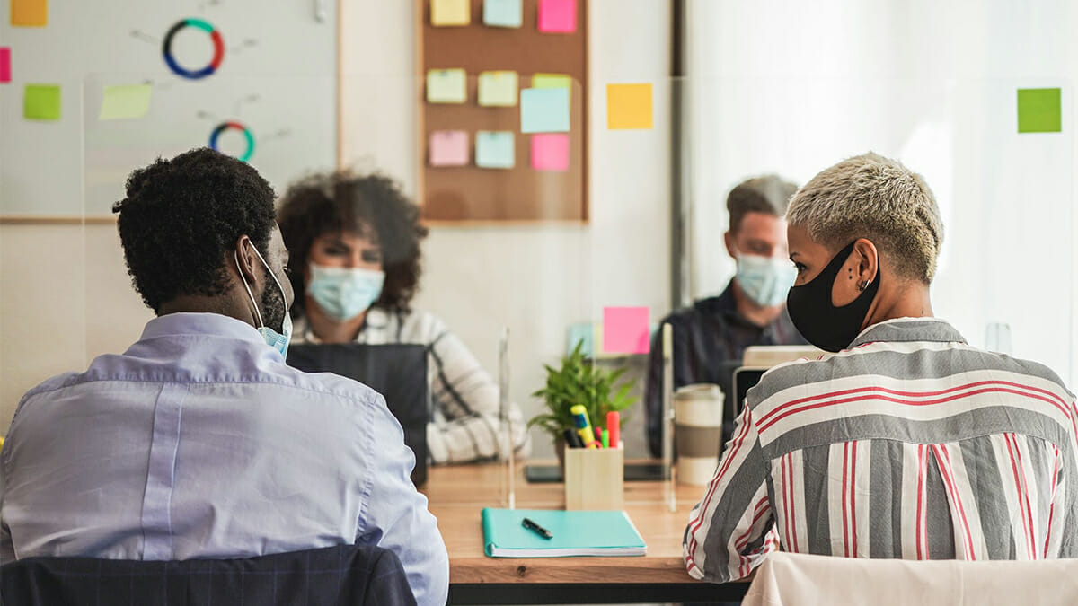 Four office workers around a table wearing masks