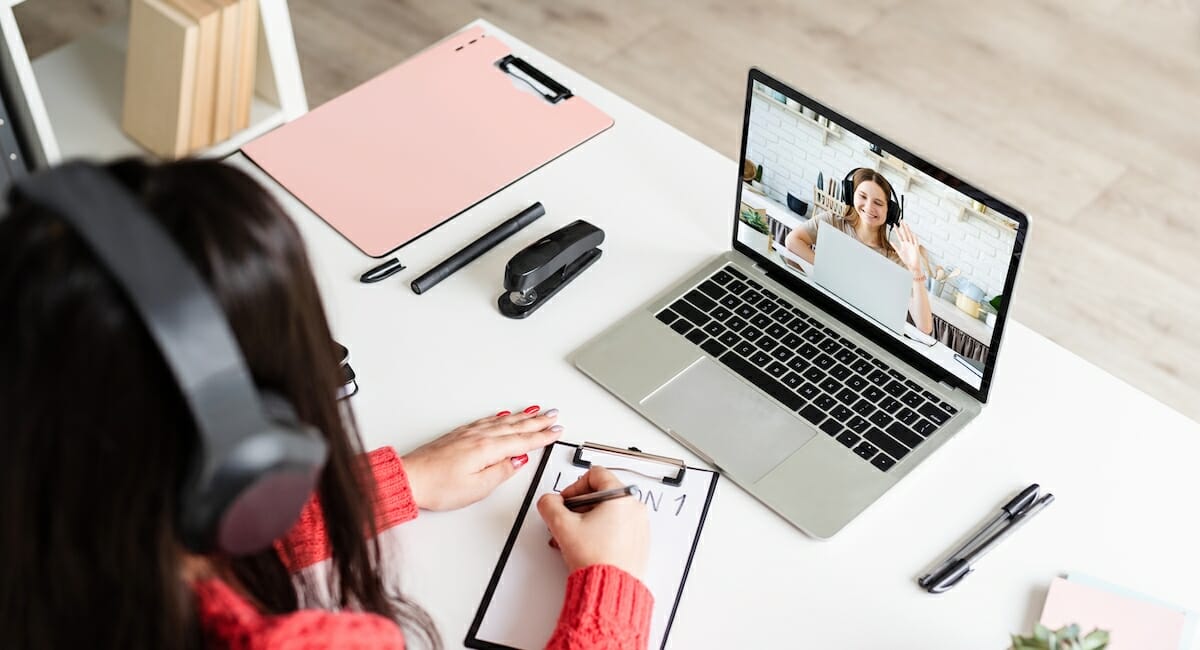 A person taking notes and watching a video on their laptop