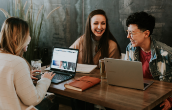 Three people talking and smiling around their computers