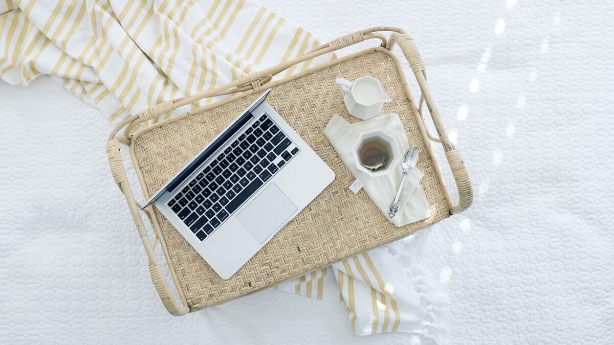 A photo of a laptop resting on a tray with coffee next to it on a bed