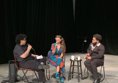 Speakers Maria Molteni and Jean Dolin in panel discussion with moderator, J.R.Uretsky. Speakers sit in a theater space.