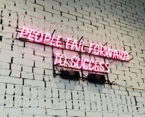 neon sign reading "People fail forward to success" on a white-washed interior brick wall