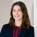 Smiling white woman with brown hair and wearing a navy blue blazer and maroon shirt