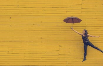 Woman holding against a yellow background holding an umbrella as if she's flying