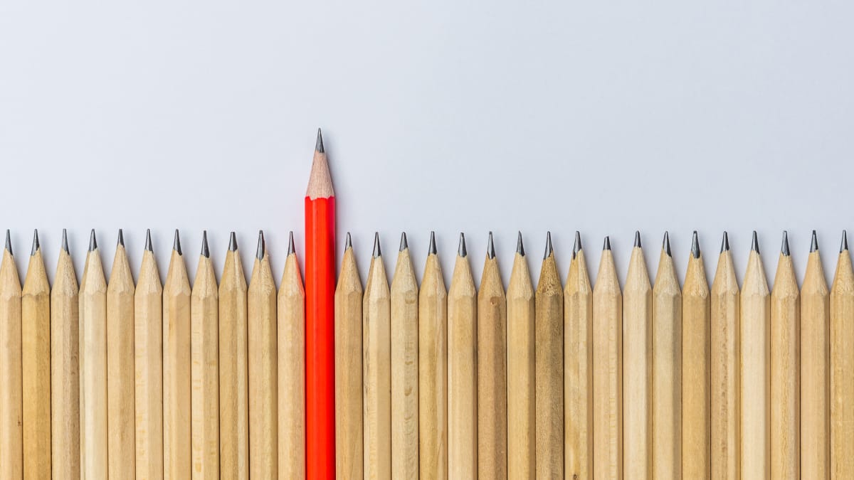 A row of similar-looking pencils with one red pencil that is pushed higher up than the rest.