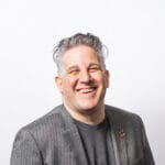 Freed_Headshot A white male with gray hair, a gray shirt, and blazer, smiling.