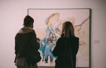 Two people wearing coats, standing in front of and looking at a painting.