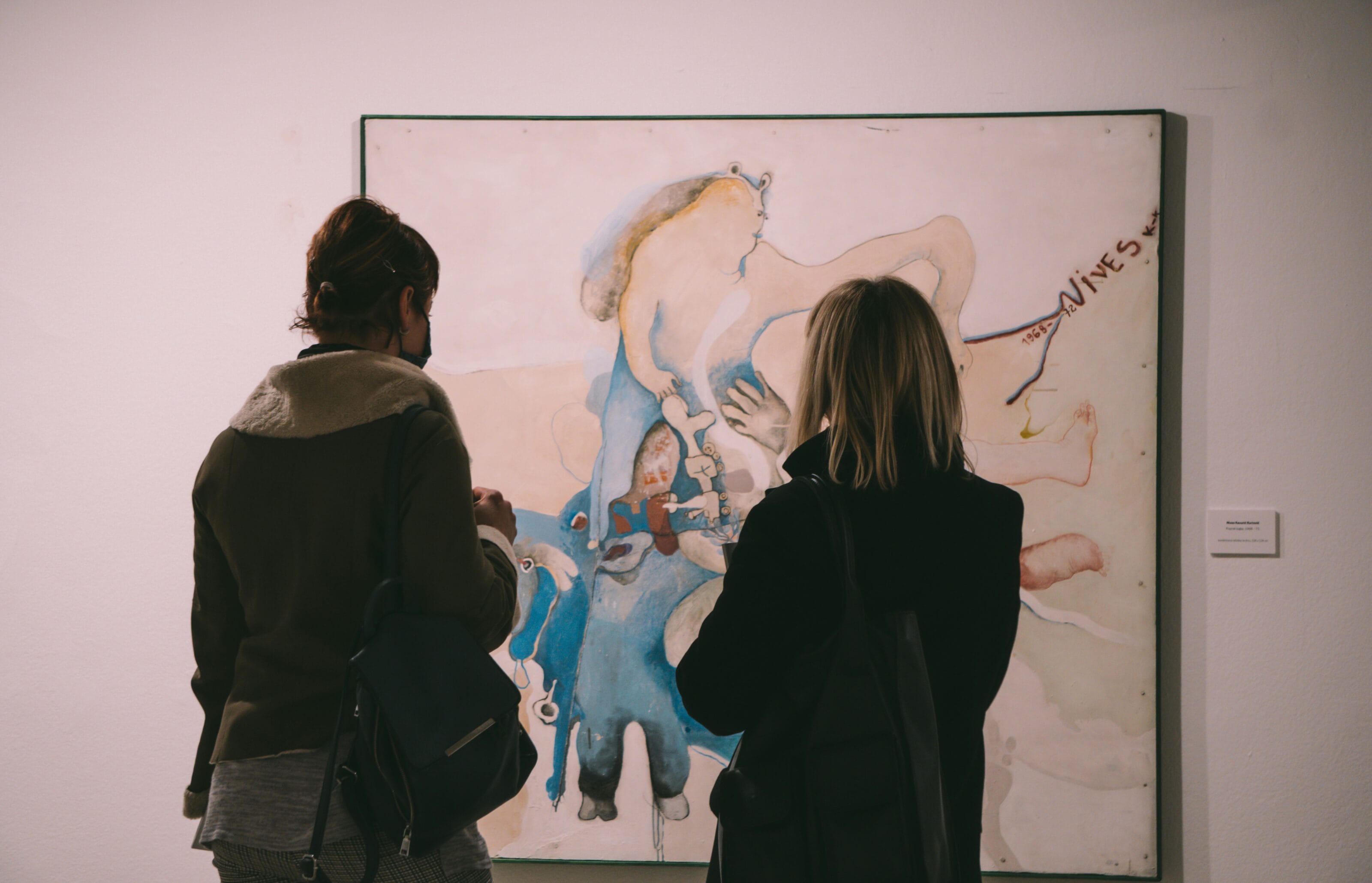 Two people wearing coats, standing in front of and looking at a painting.