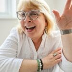 White woman with blonde hair and glasses wearing a white shirt and smiling