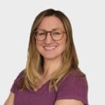 Blonde-haired woman with glasses wearing a magenta, short-sleeved t-shirt