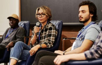 Three young people seated in armchairs, holding a microphone.