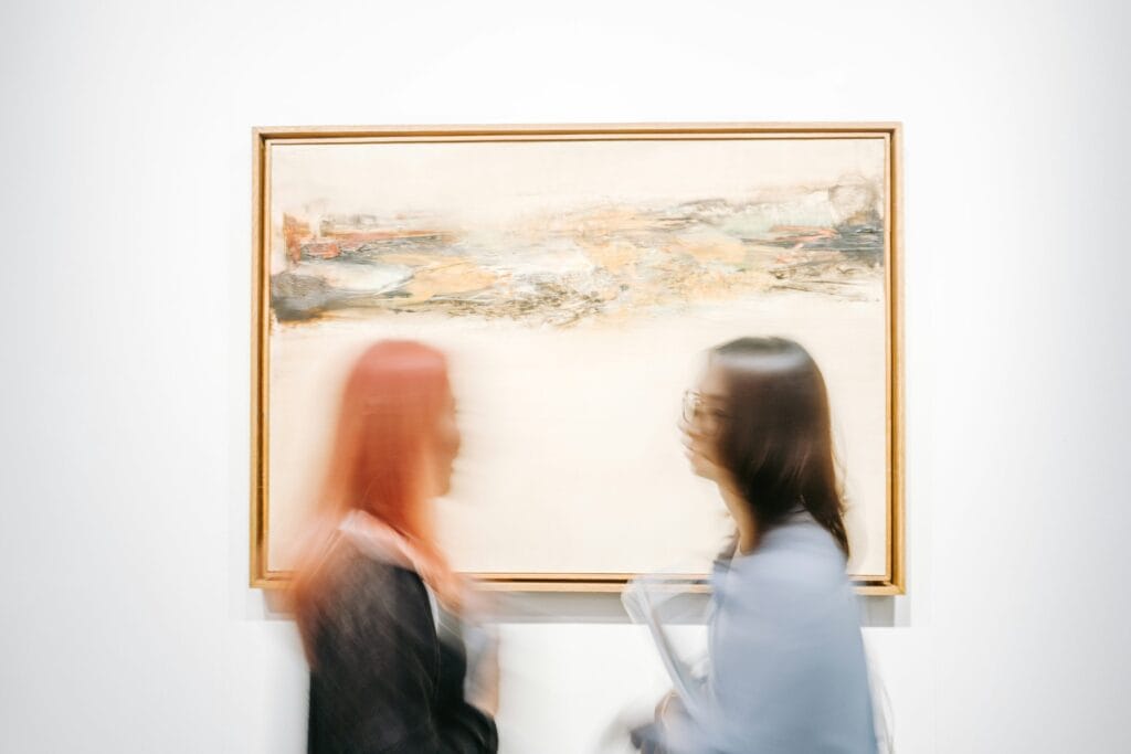 Two people wearing coats, standing in front of and looking at a painting.