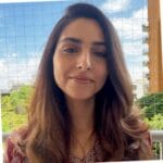 Brown-haired woman with brown eyes and a pink shirt smiling in front of a pastoral background.