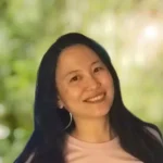 Dark-haired asian woman, smiling and wearing a light pink t-shirt.