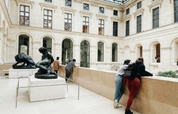 people in a white-stone museum space standing next to figurative sculptures.
