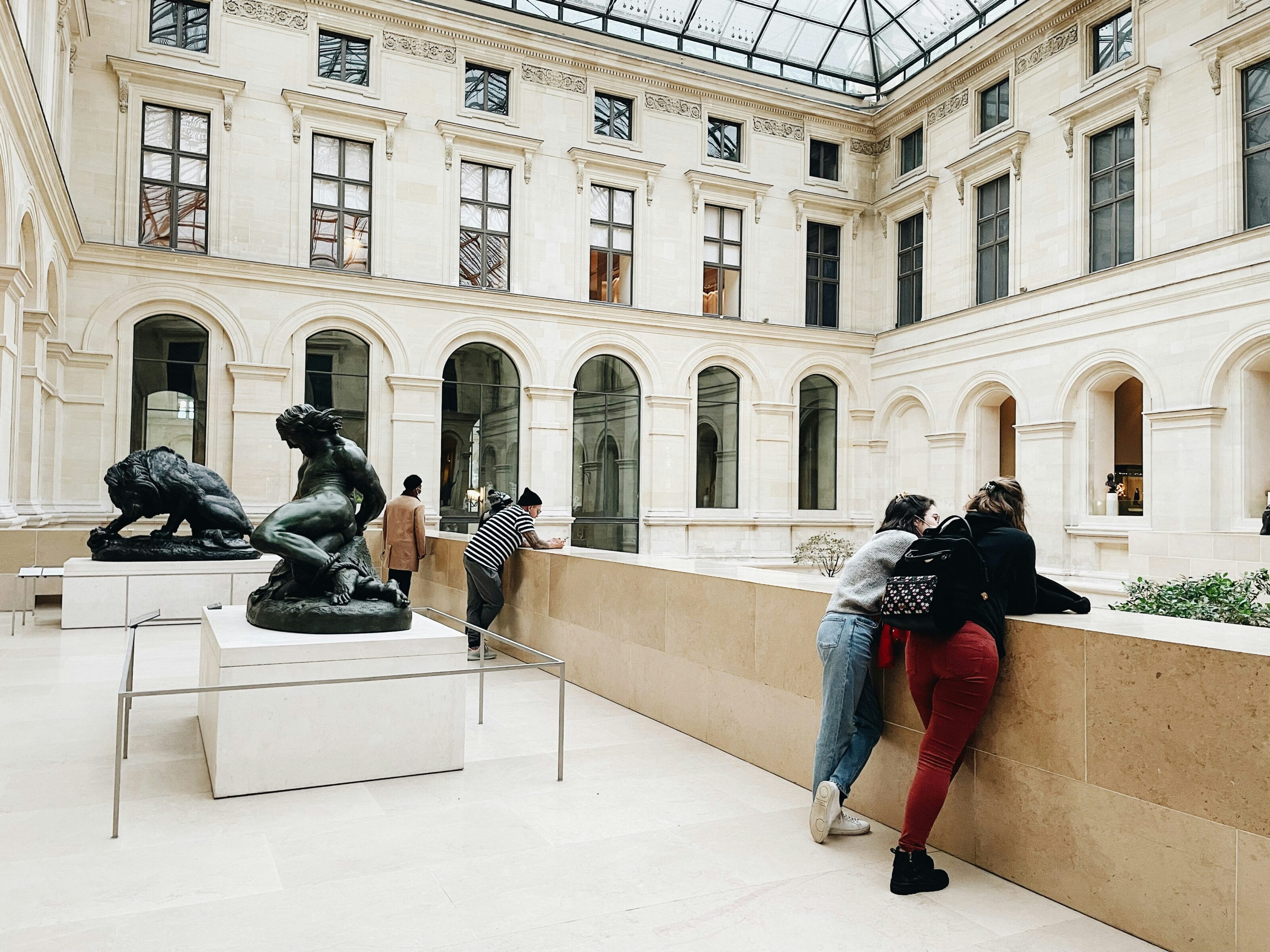 people in a white-stone museum space standing next to figurative sculptures.