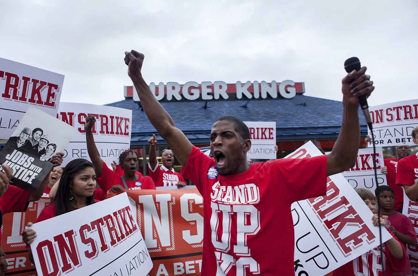 BIPOC individuals wearing red t-shirts reading "Stand Up KC" stand in a group protest in front of a Burger King.