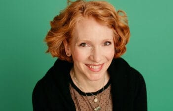 Headshot of Kendra Roberts smiling, wearing a dark blazer over a light top, set against a teal backdrop.