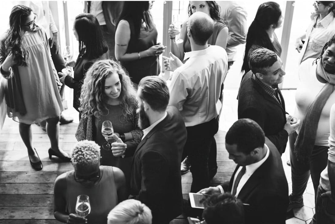 A group of design professionals gathered in a dimly lit, atmospheric venue, engaged in casual conversation.