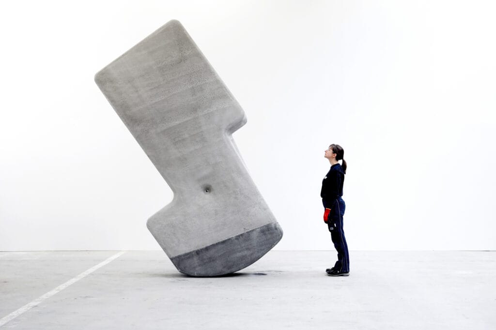 A person stands inside the hollow silhouette cutout of a tall, grey stone structure against a plain white background.