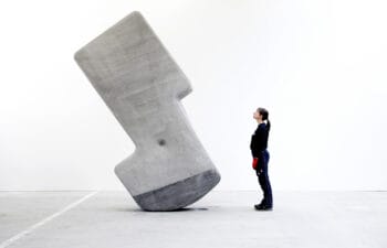 A person stands inside the hollow silhouette cutout of a tall, grey stone structure against a plain white background.