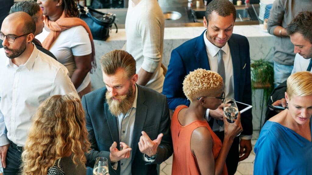 A group of people dressed in business casual attire gathered and conversing in a dimly lit, atmospheric venue with soft lighting.