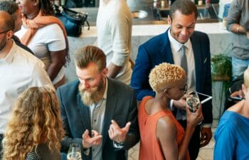 A group of people dressed in business casual attire gathered and conversing in a dimly lit, atmospheric venue with soft lighting.
